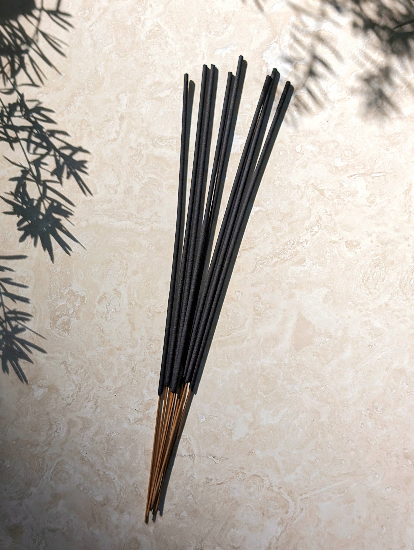 Black incense sticks on a light stone surface with greenery