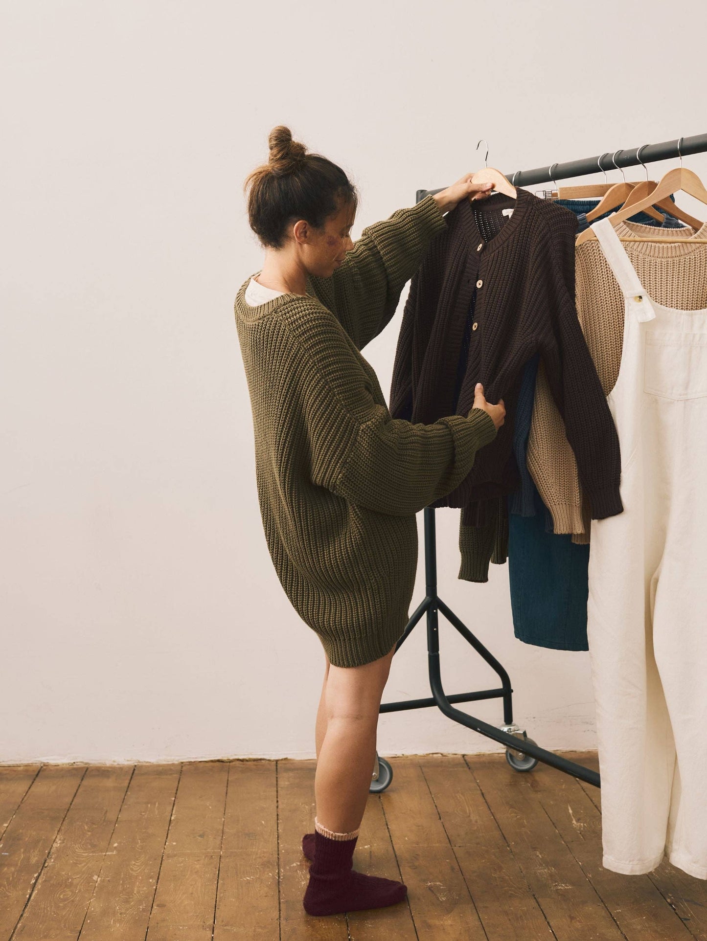 Person organizing clothes on a rack against a white wall.