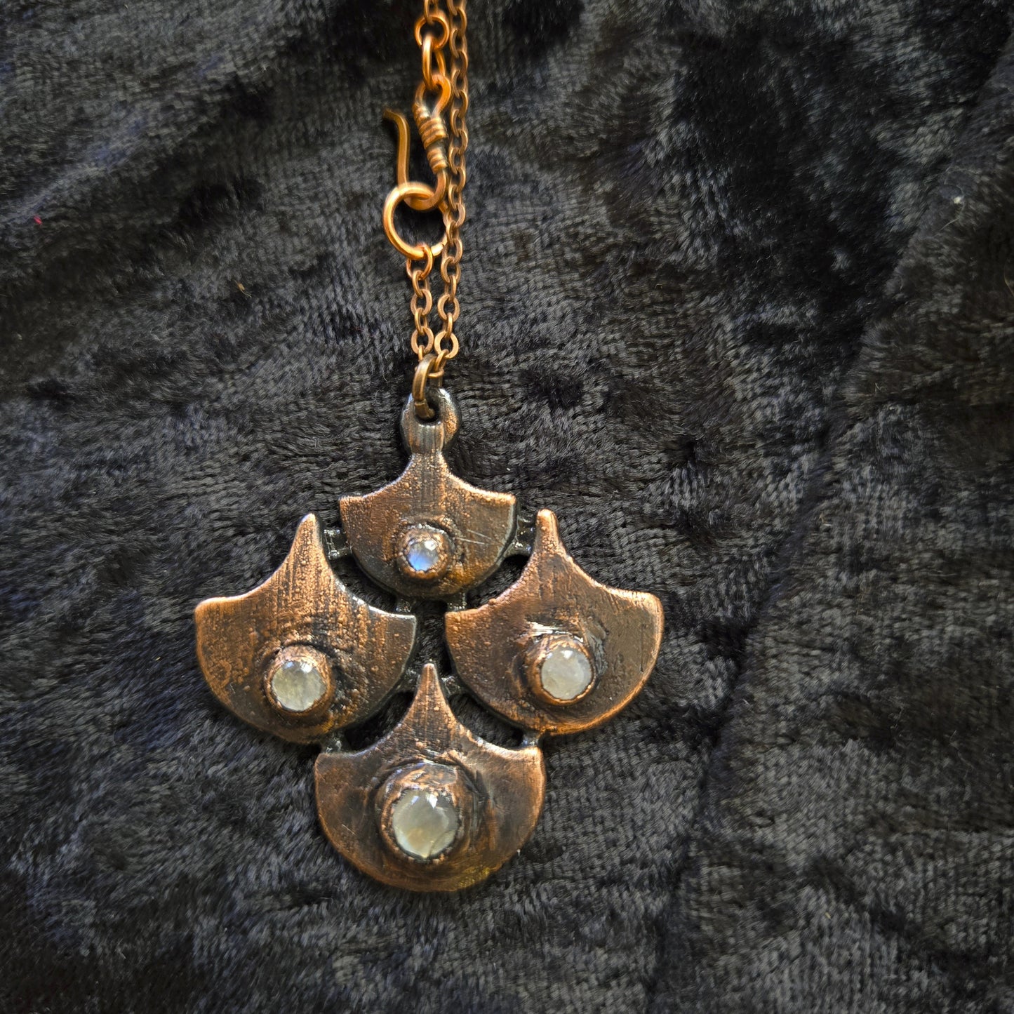 Copper necklace with four leaf-like pendants on a dark textured background