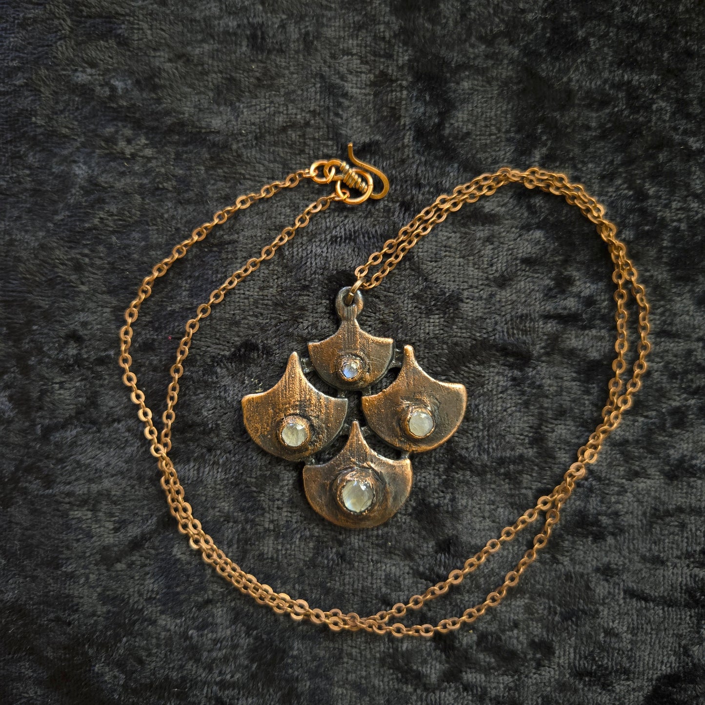 Copper chain necklace with leaf-like pendants on a textured black background