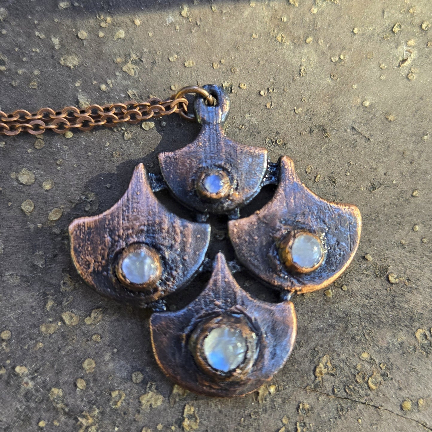 Metallic necklace with moonstone and a unique shield design on a textured surface