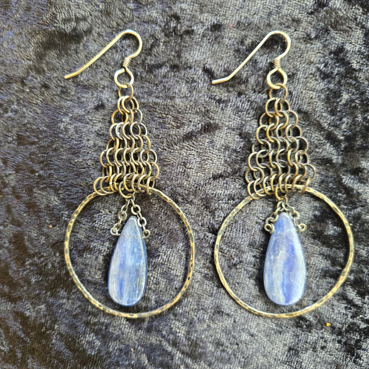 Pair of gold hoop earrings with blue teardrop stones on a textured gray background