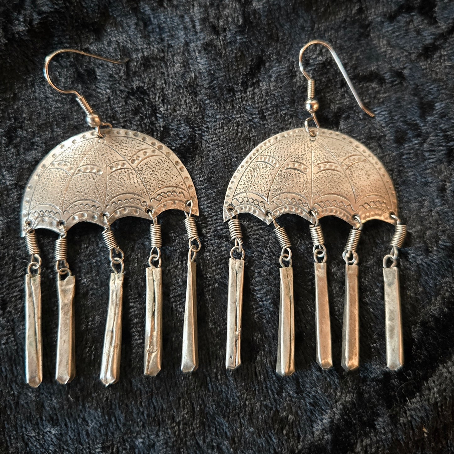 Pair of silver earrings with intricate designs on a dark textured background