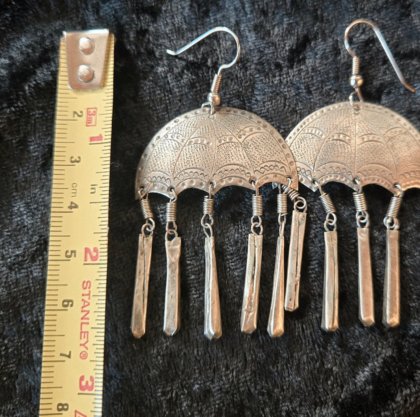 Pair of silver earrings with intricate designs on a dark background, accompanied by a ruler for scale.