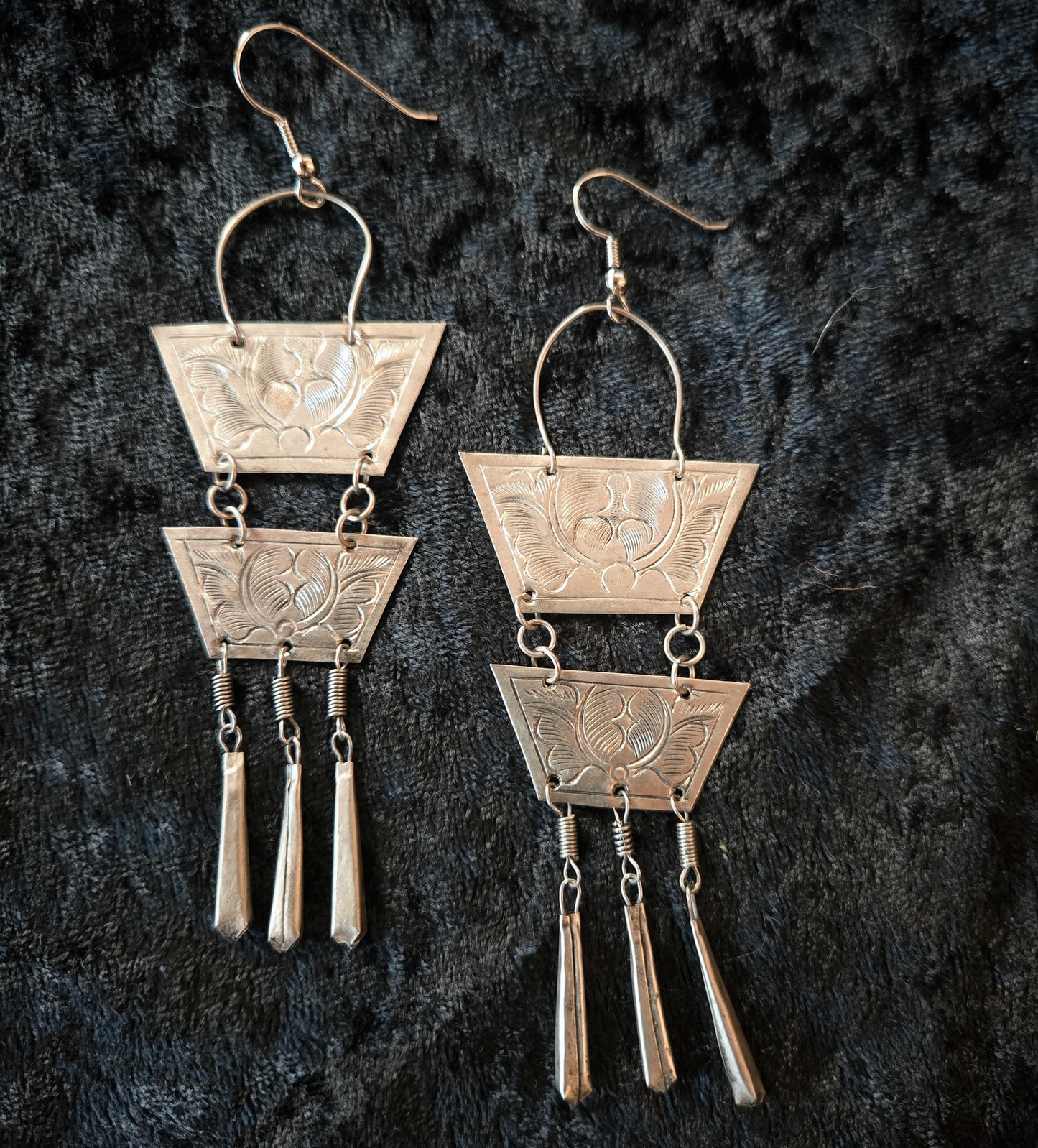 Pair of silver earrings with geometric design on a dark textured background