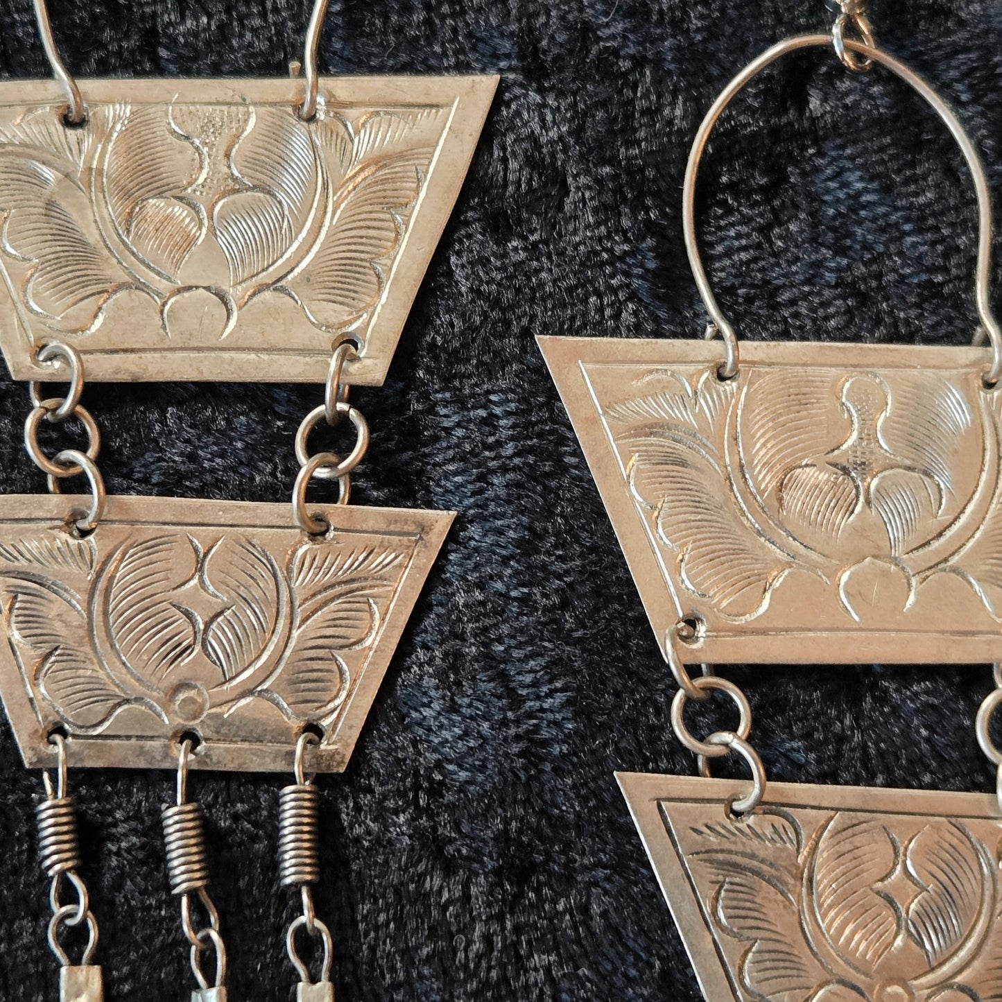 Pair of silver earrings with geometric designs on a dark textured background