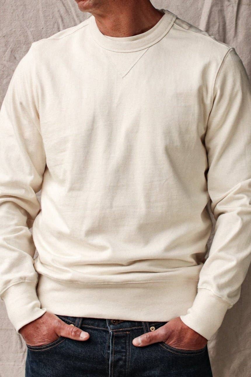 Person wearing a beige sweatshirt with hands in pockets against a neutral background