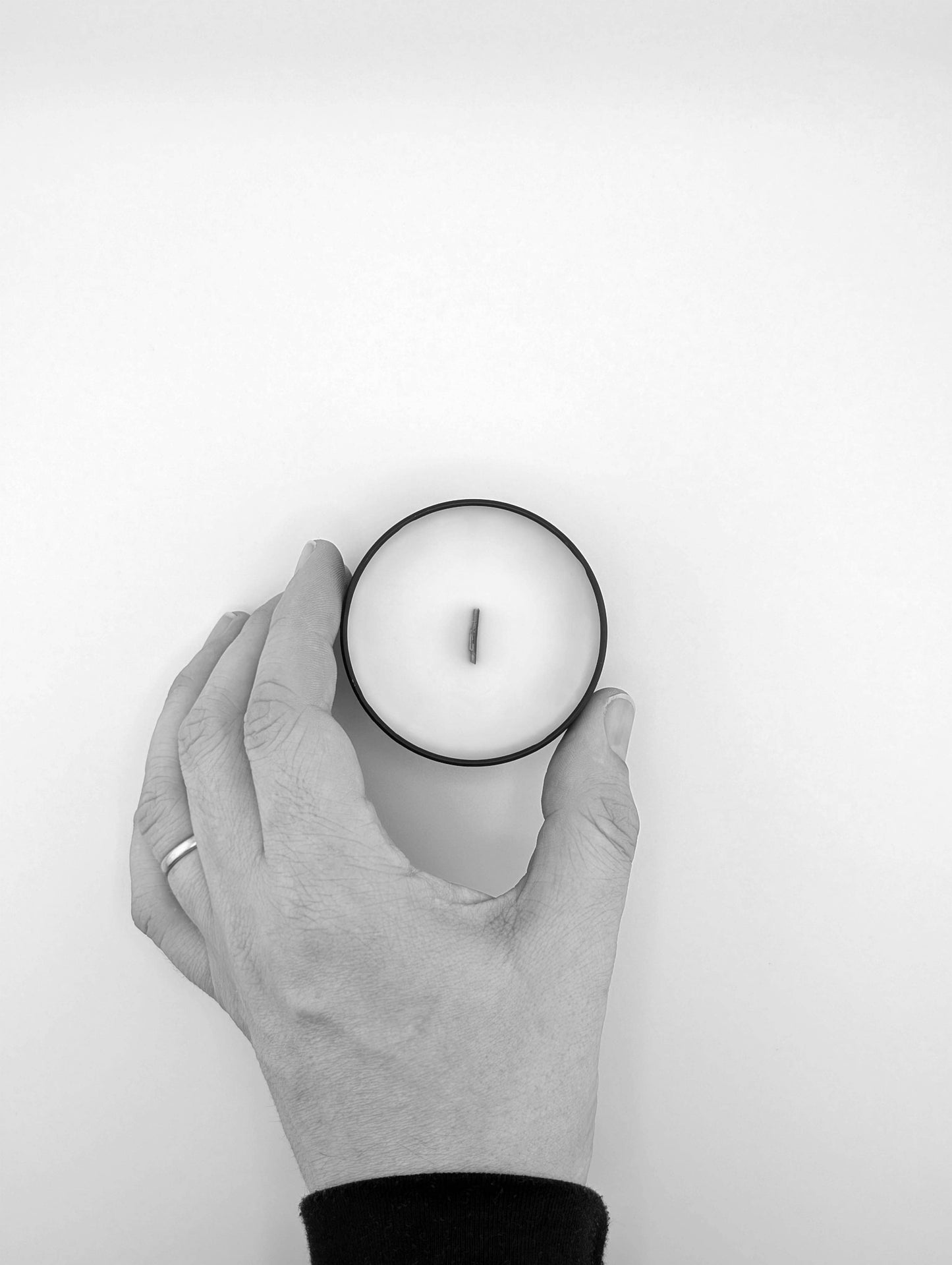 Hand holding a white candle against a white background