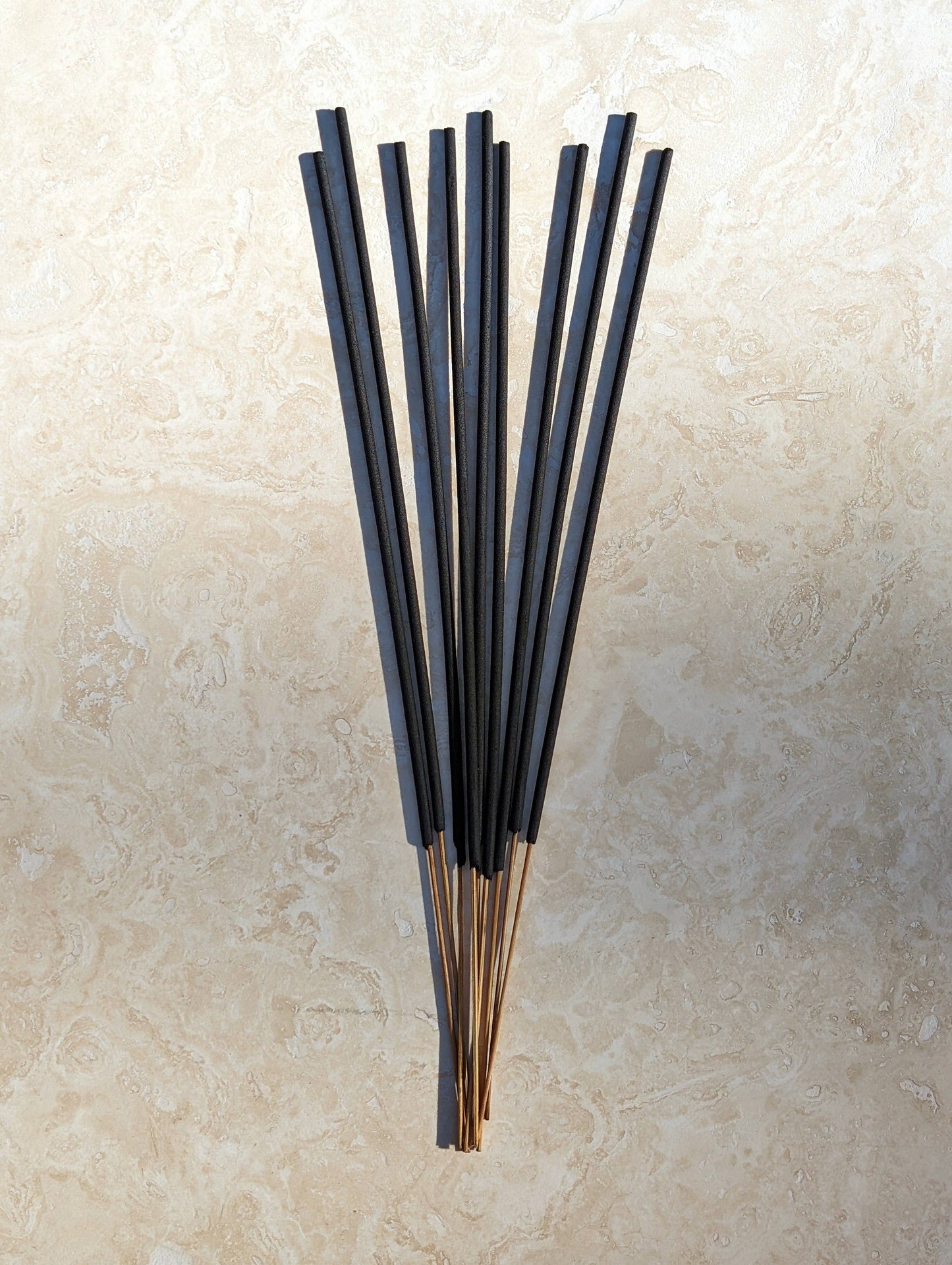 Set of black incense sticks on a beige stone surface