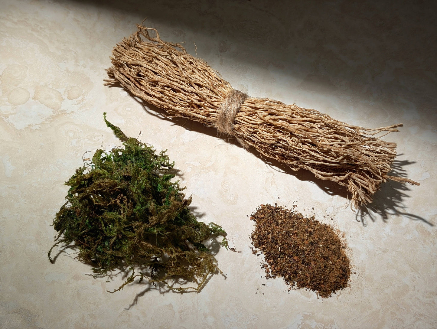 Bundled herbs, a clump of green plants, and a pile of brown material on a textured surface.