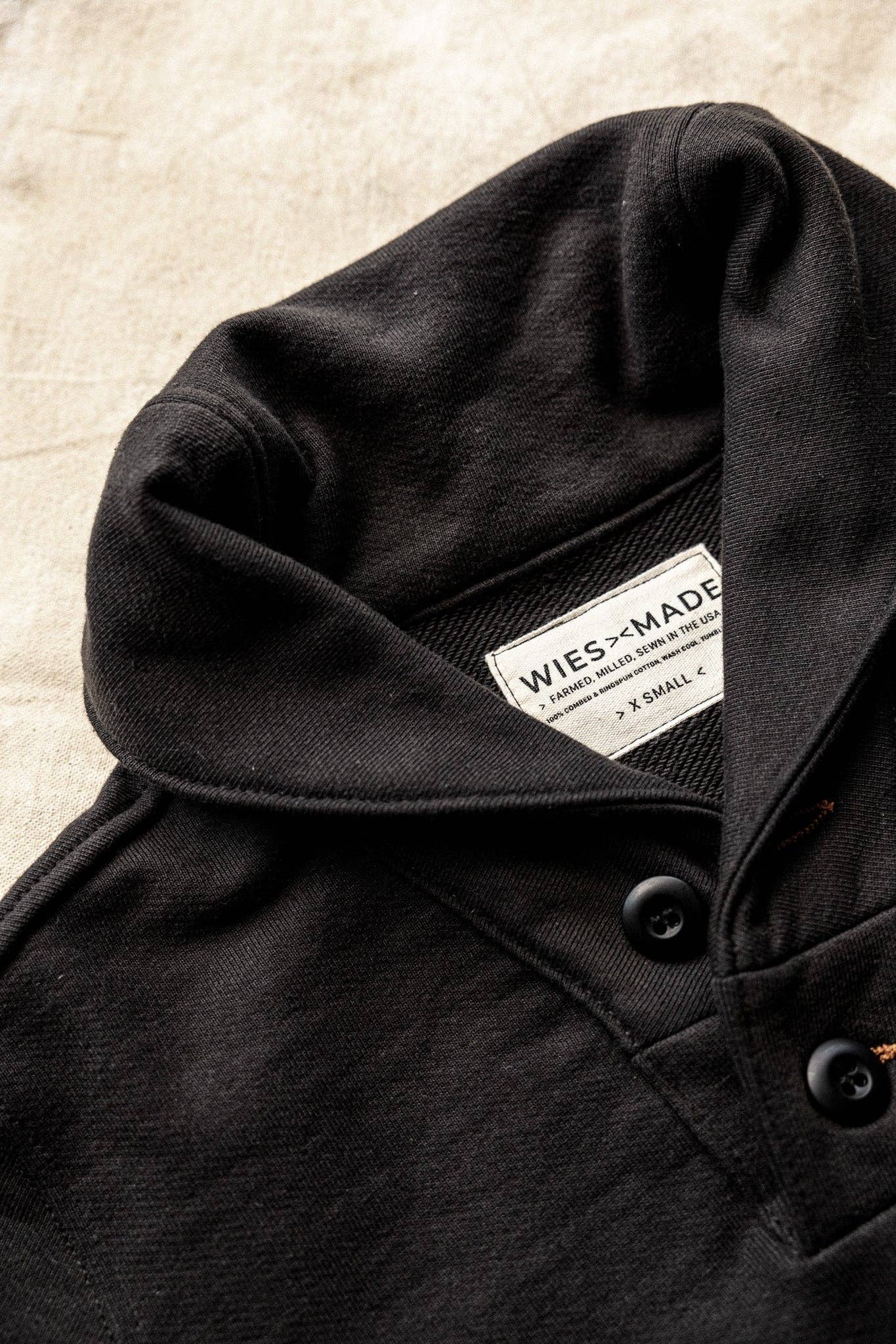 Close-up of a black coat with a visible brand label on a textured beige background