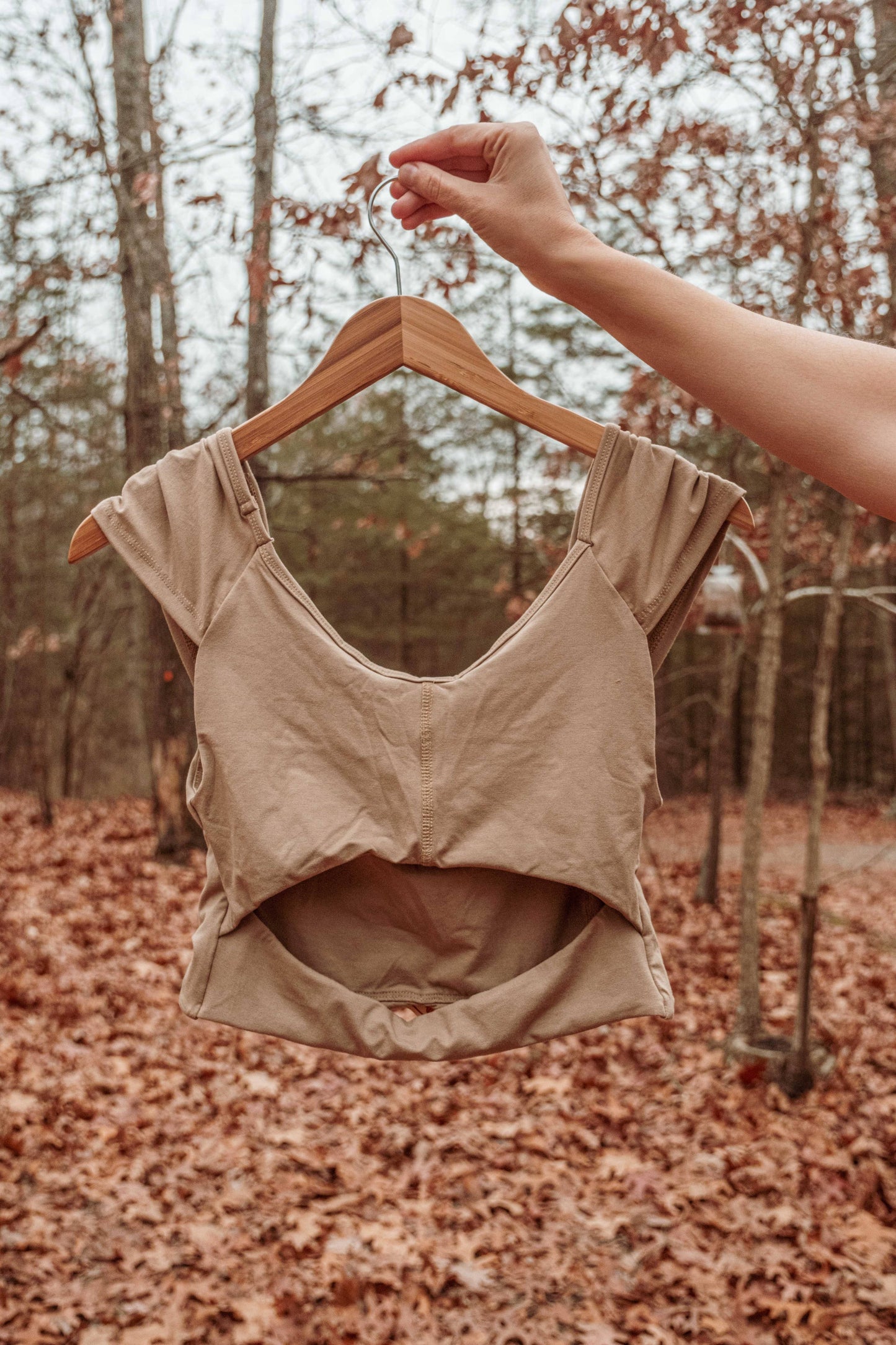 Beige crop top on a hanger against a forest background