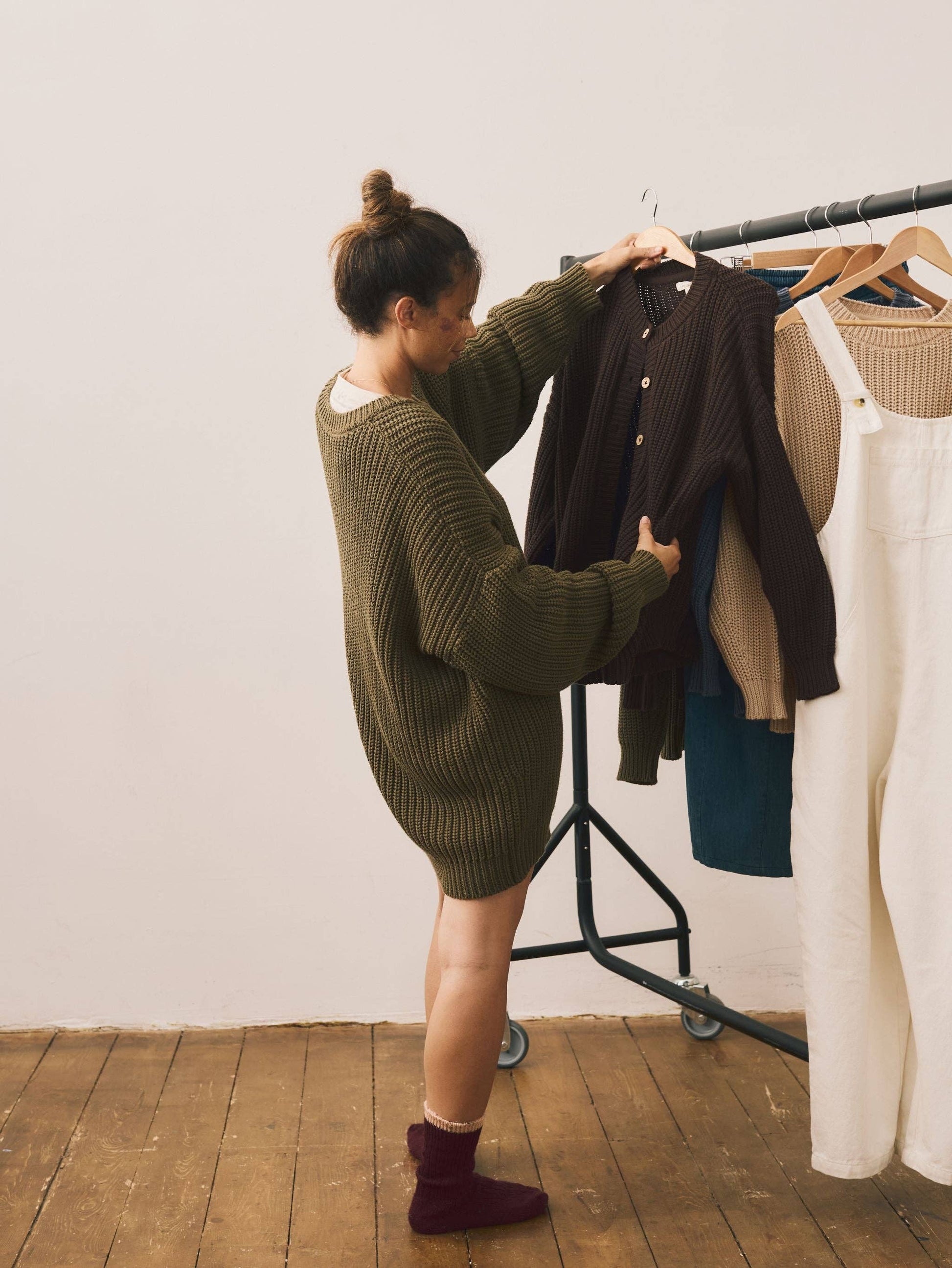 Person organizing clothes on a rack against a white wall.