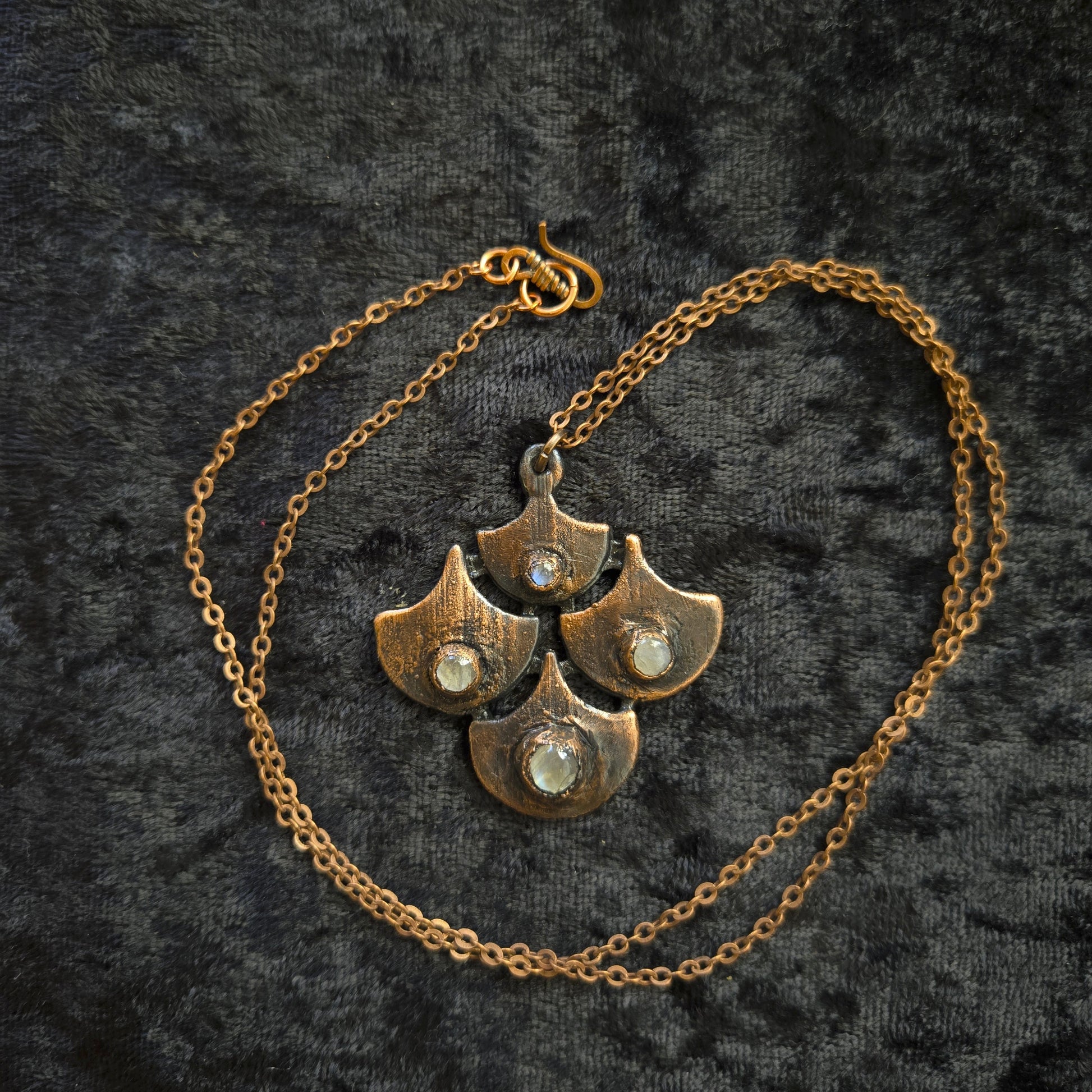 Copper chain necklace with leaf-like pendants on a textured black background