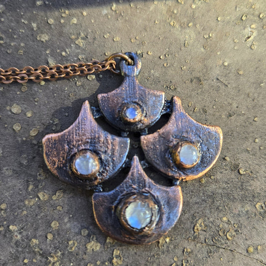 Metallic necklace with moonstone and a unique shield design on a textured surface