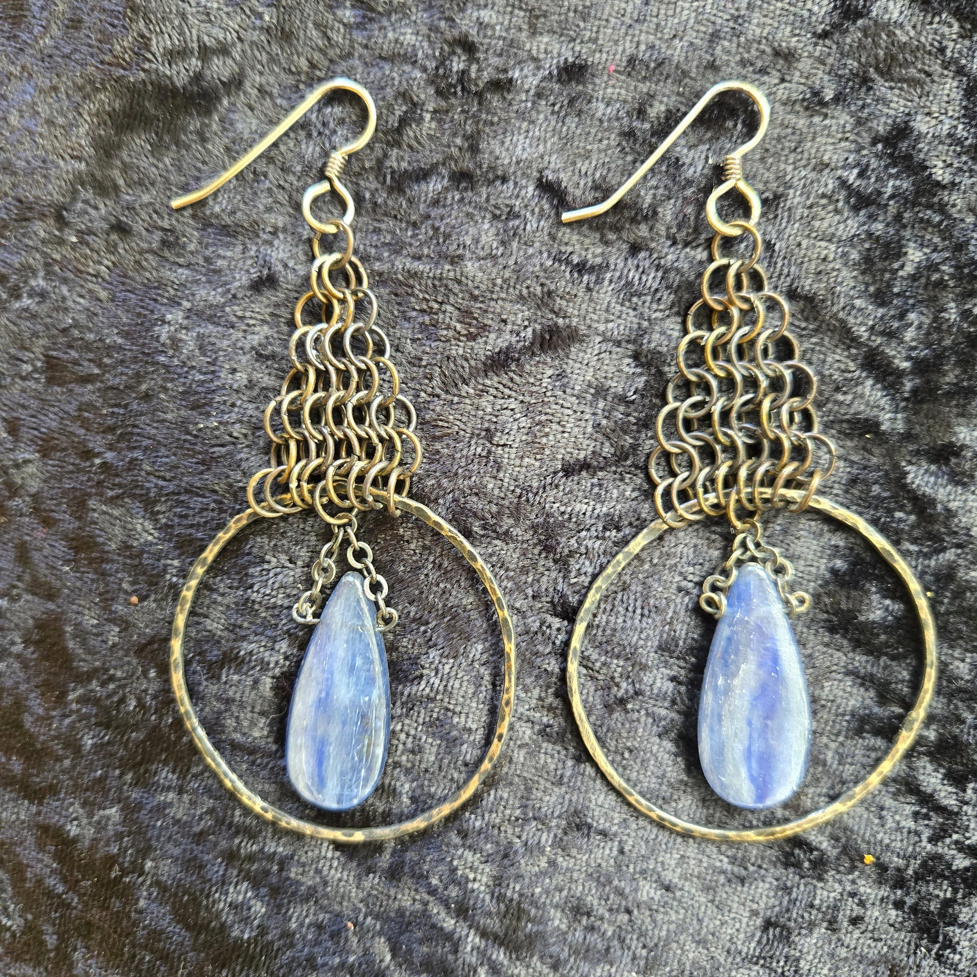 Pair of gold hoop earrings with blue teardrop stones on a textured gray background
