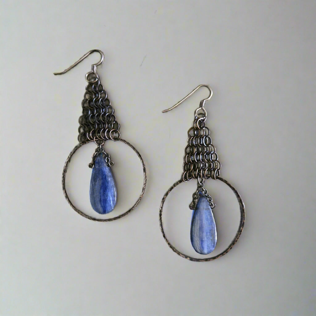 Pair of silver hoop earrings with blue teardrop stones on a metallic surface