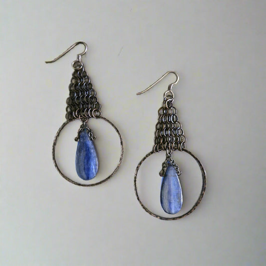 Pair of silver hoop earrings with blue teardrop stones on a metallic surface