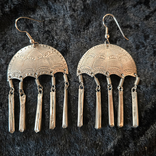 Pair of silver earrings with intricate designs on a dark textured background