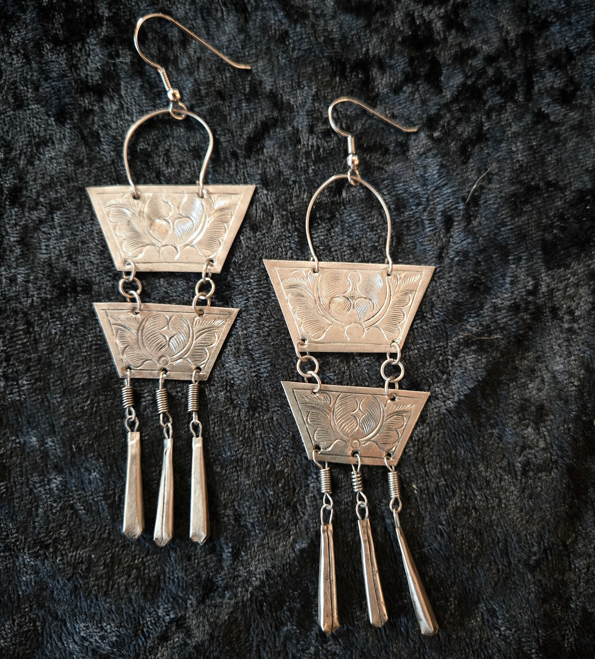 Pair of silver earrings with geometric design on a dark textured background