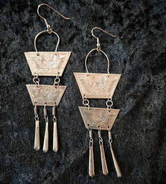 Pair of silver earrings with geometric design on a dark textured background
