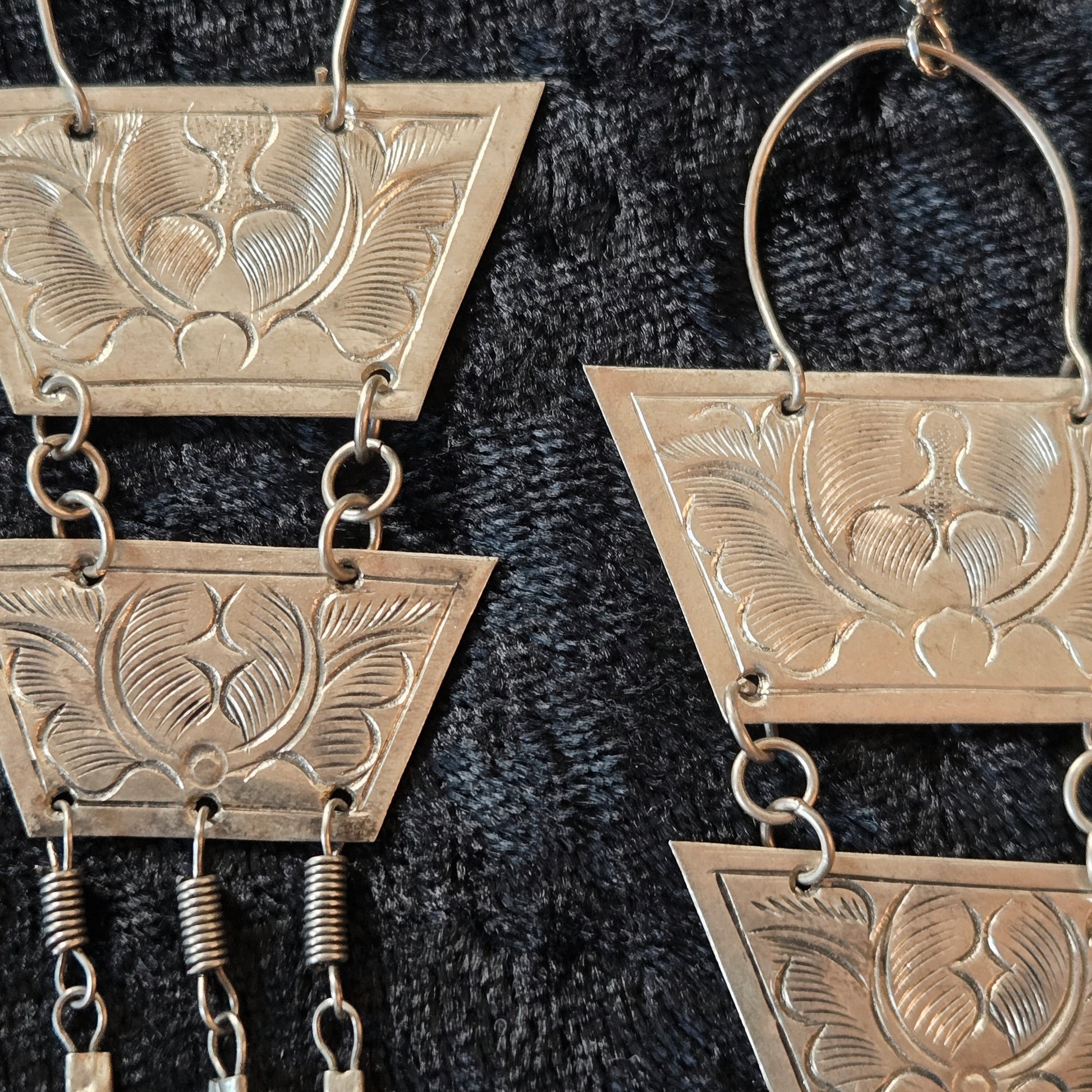 Pair of silver earrings with geometric designs on a dark textured background