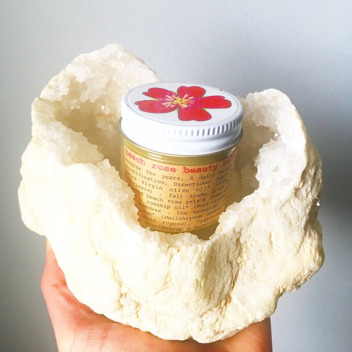 Jar of beach rose beauty product held inside a large white stone