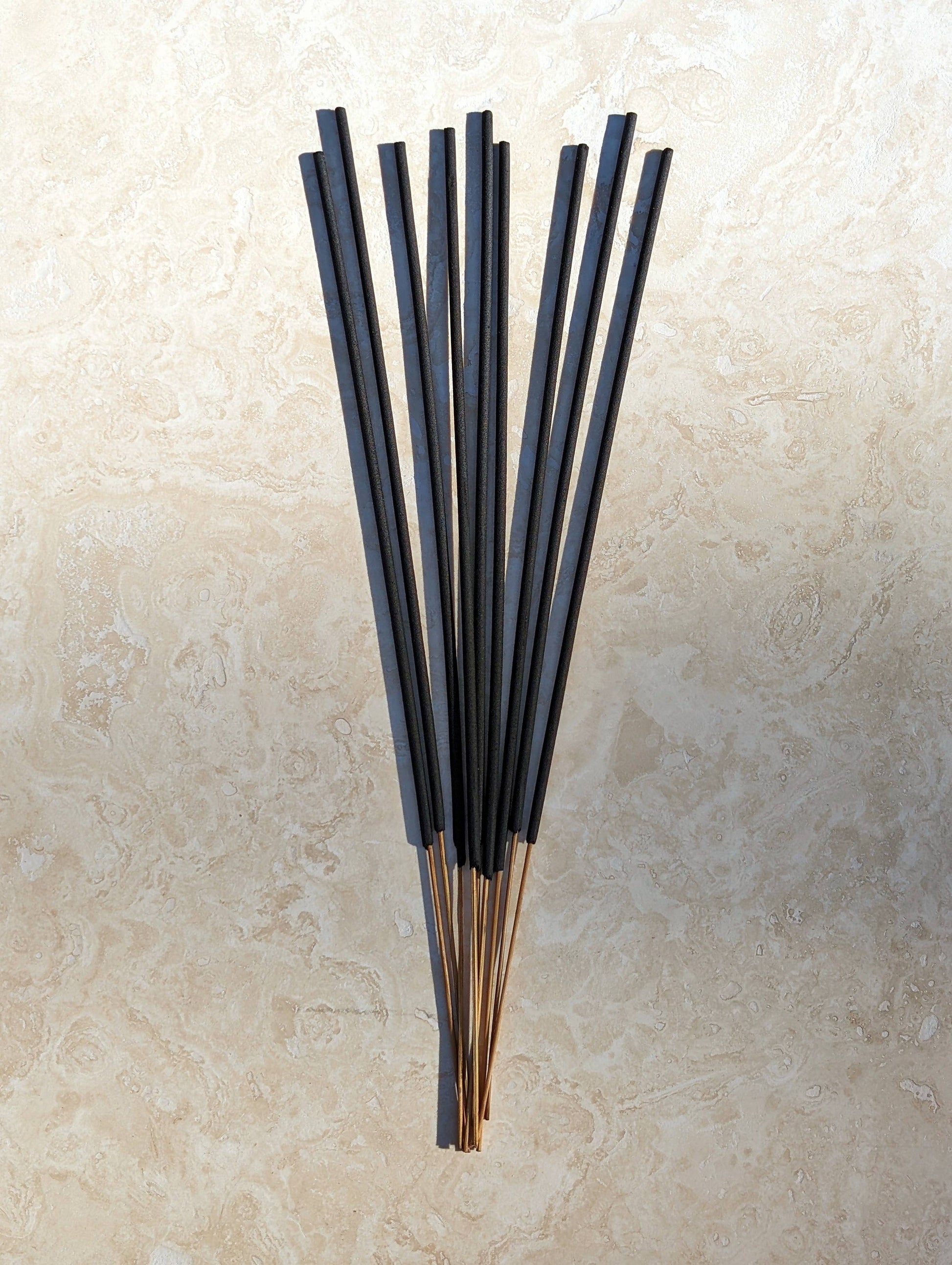 Set of black incense sticks on a beige stone surface