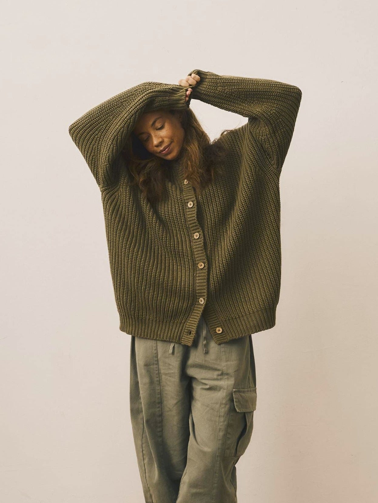 Person wearing a green ribbed sweater and matching pants against a white wall.
