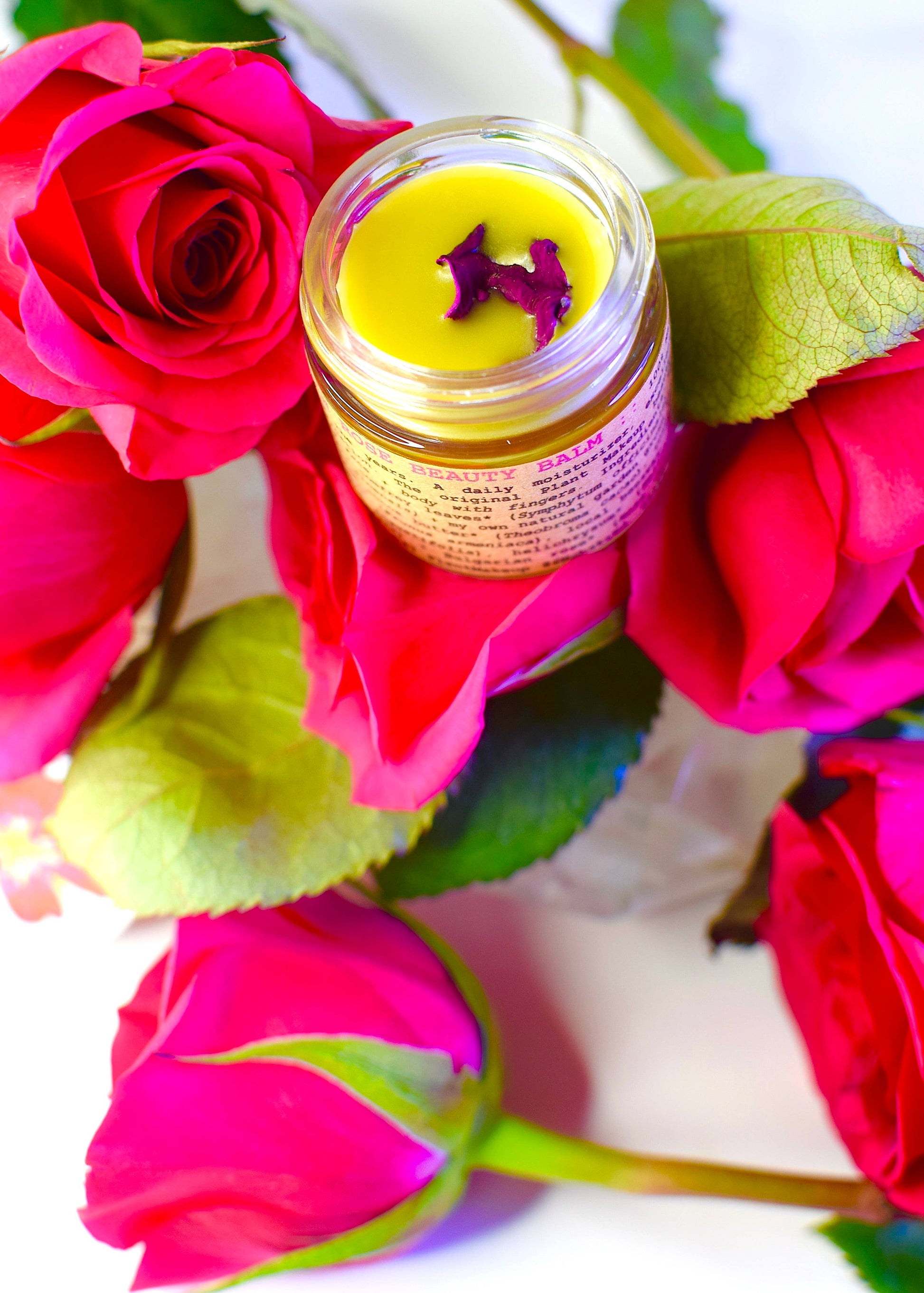 Jar of cream with a yellow lid surrounded by pink roses