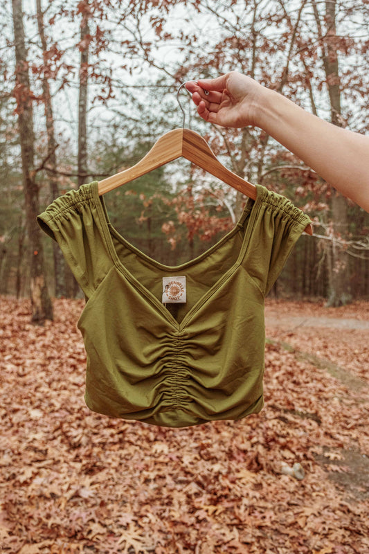 Green crop top on a hanger against a forest background with fallen leaves